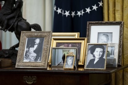 Framed family photographs on the table behind the Resolute Desk in the Oval Office, including a black-and-white portrait of Donald Trump with his father Fred Trump.